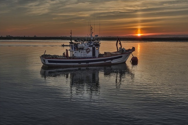 Fishing boat on body of water with sunset in background